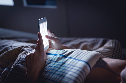 Eine Person liegt im Bett und tippt auf dem Display ihres Smartphones.