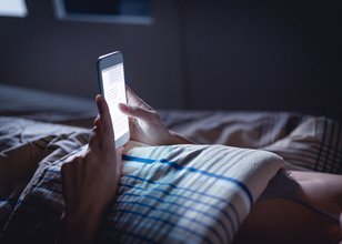 Eine Person liegt im Bett und tippt auf dem Display ihres Smartphones.